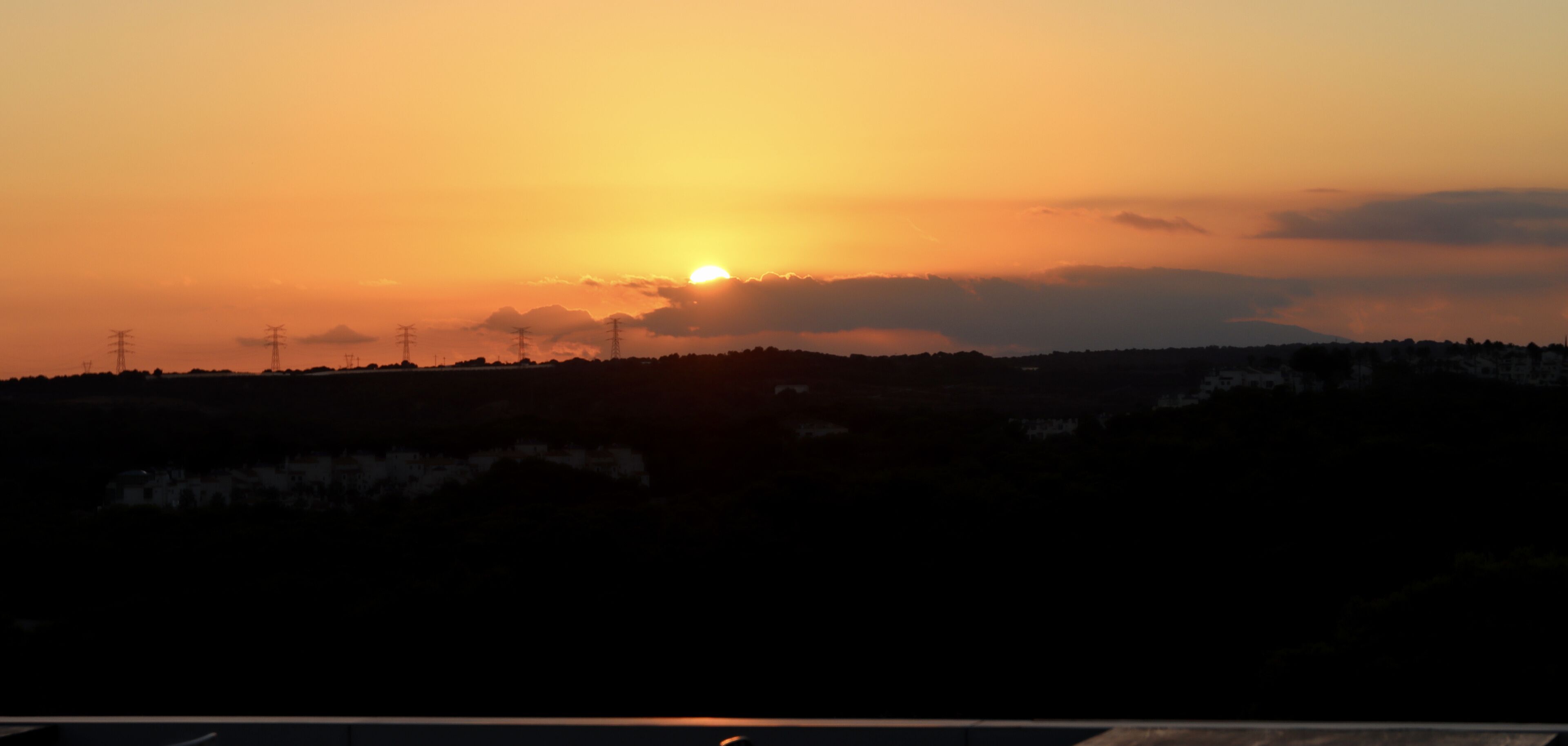 A sunset over a landscape with power lines and a silhouette of buildings.