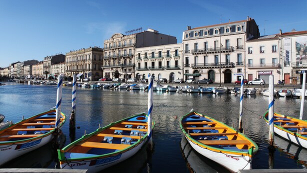 Un port de plaisance où sont amarrés des bateaux aux couleurs vives, des bâtiments dotés de balcons et un ciel d’un bleu limpide.