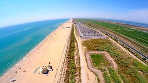 Vue aérienne d’une plage avec un parking, une route et des champs verdoyants.