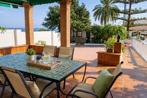 An outdoor patio with a table set for dining, surrounded by chairs, and a view of the sea.