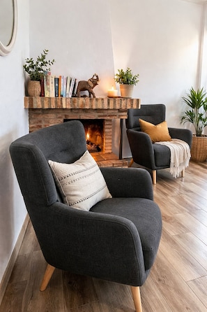 A cozy living room with a fireplace, two armchairs, and a bookshelf.