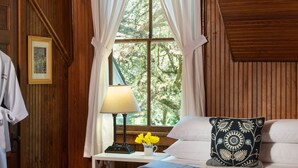 A wooden-paneled room with a bed, a nightstand with a lamp, a vase with flowers, and a framed picture on the wall. - Magnolia Springs B&B (Magnolia Springs)