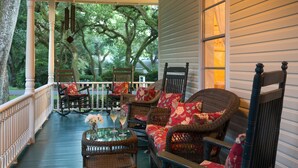A porch with wicker furniture, a glass table with a vase and wine glasses, and a view of trees through the windows. - Magnolia Springs B&B (Magnolia Springs)