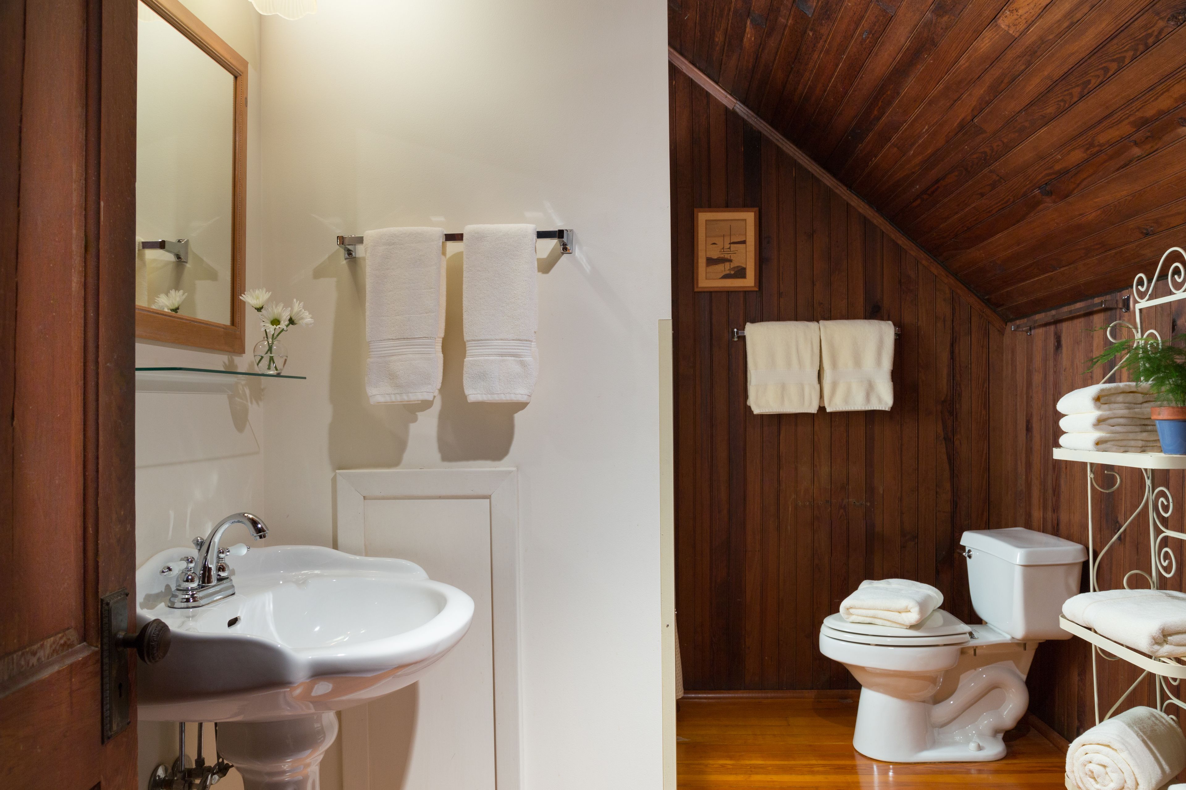 Une salle de bain avec un plafond en bois, un lavabo blanc, des toilettes et une étagère avec des serviettes.