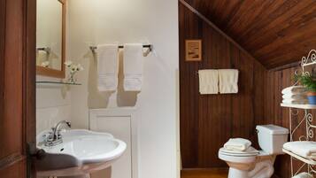 A bathroom with a wooden ceiling, a white sink, a toilet, and a shelf with towels.