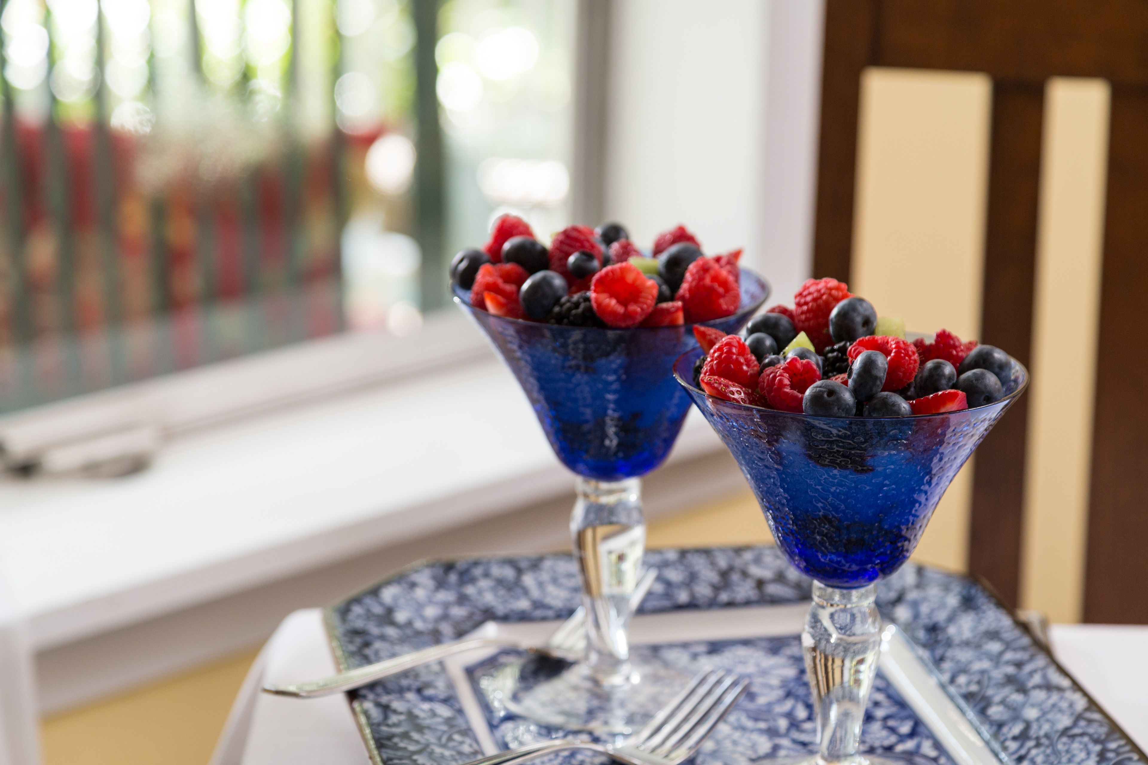 Dos cuencos de vidrio azul llenos de bayas variadas sobre una mesa con mantel estampado.