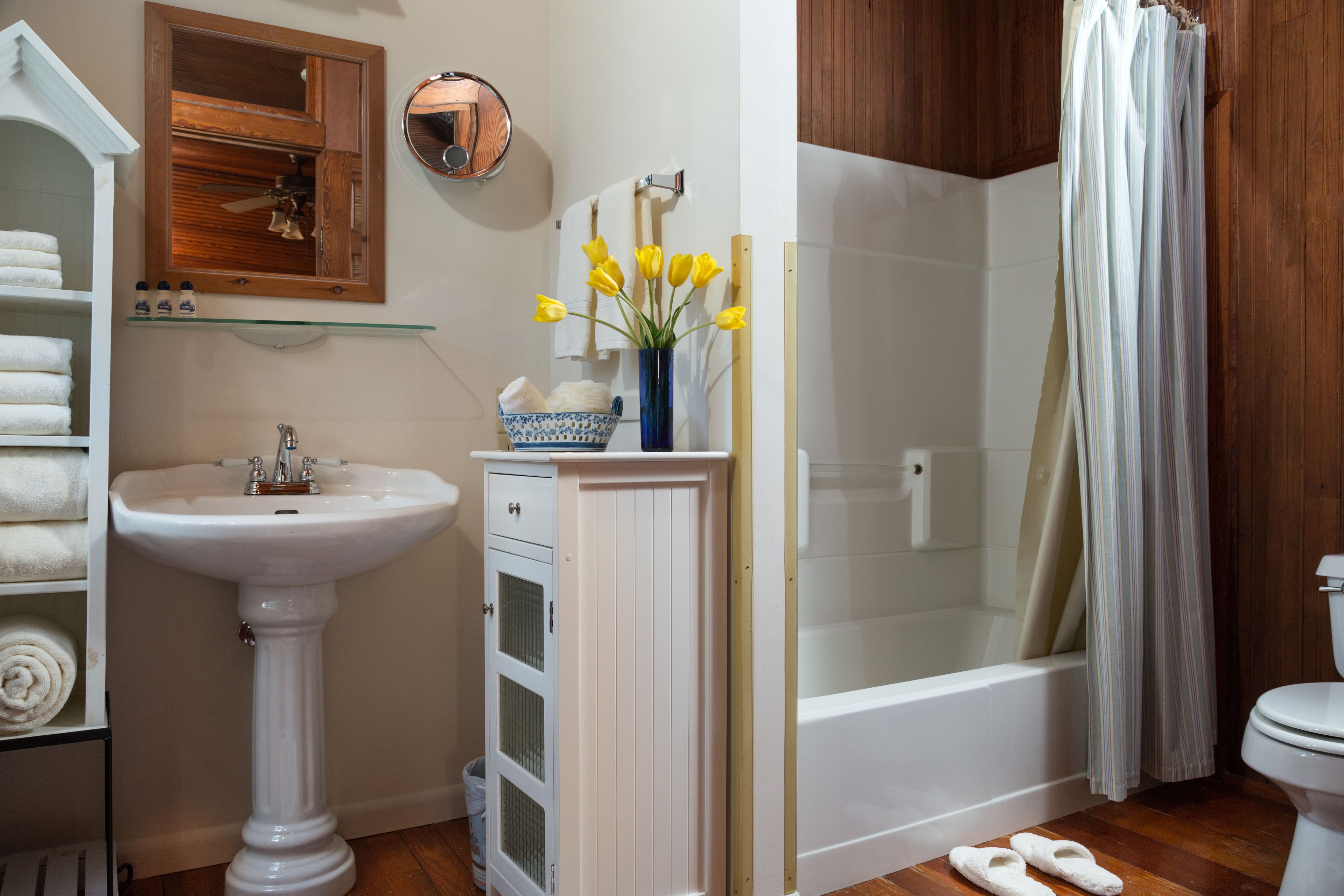 Un baño con lavamanos pedestal, espejo, toallero, ducha con cortina y retrete.