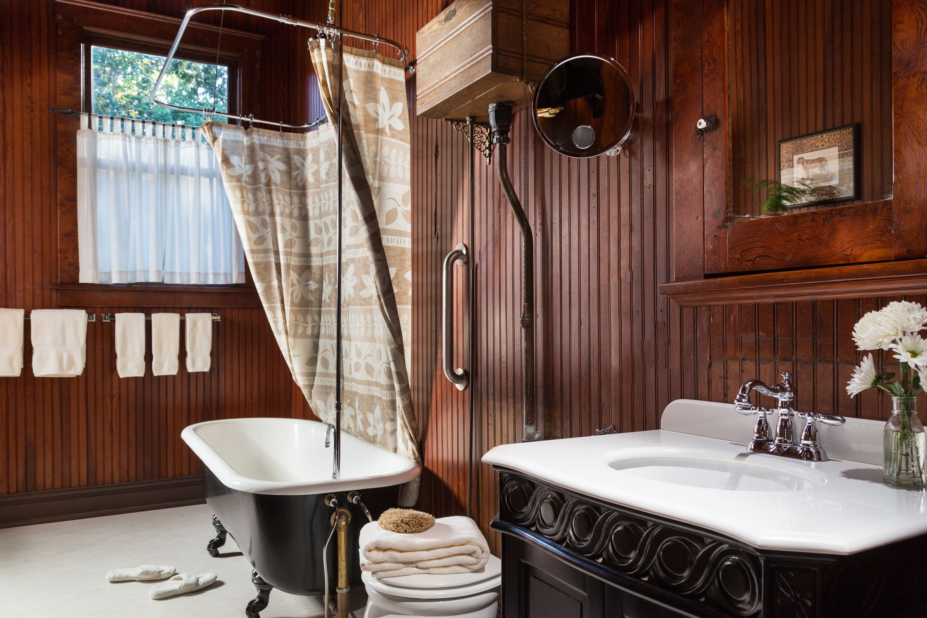 A bathroom with a bathtub, a sink, and a toilet. There are towels hanging on the wall and a window with curtains.