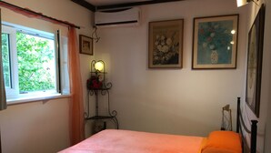 Un dormitorio con cama, ventana, aire acondicionado de pared y cuadros enmarcados.