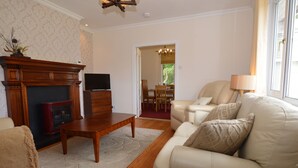 A living room with a fireplace, a television, a sofa, and a dining area visible through an open door. - Cedar Cottage at Rashfield nr Dunoon-sleeps up to 6-Pet Friendly(1 max) (Dunoon)