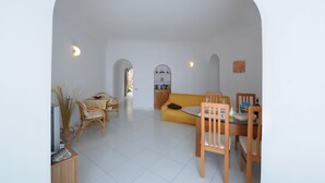 Ein modernes Wohnzimmer mit einer Couch, einem Esstisch und Stühlen. Ein Fernseher und eine Pflanzvase sind ebenfalls vorhanden.