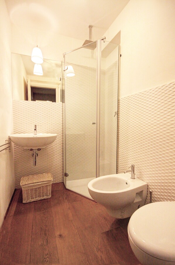 A bathroom with a wooden floor, a white sink, a bidet, and a glass shower enclosure. - Palazzo Bichi Ruspoli-Historical Res, near Campo Square and close to everything (Siena)