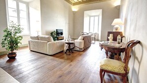 Ein Wohnzimmer mit Sofa, Sessel, Esstisch aus Holz und einer Zimmerpflanze.