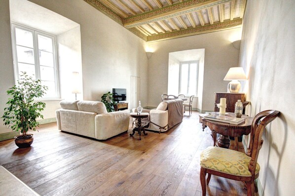A living room with a sofa, armchair, wooden dining table, and a potted plant. - Palazzo Bichi Ruspoli-Historical Res, near Campo Square and close to everything (Siena)