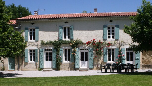 A two-story building with a red-tiled roof, green shutters, and a gravel driveway. - Spacious farmhouse with private large heated enclosed pool and extensive grounds (Lempaut)