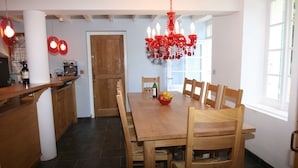 A dining area with a wooden table and chairs, a chandelier, and a kitchen area with a wooden door and counter. - Spacious farmhouse with private large heated enclosed pool and extensive grounds (Lempaut)