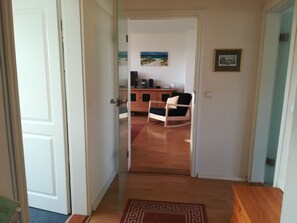 Un pasillo que conduce a una sala de estar con piso de madera, una mecedora, una mesa de centro y un cuadro en la pared.