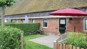 Una casa de ladrillo con tejado de paja, un paraguas rojo y un patio empedrado.
