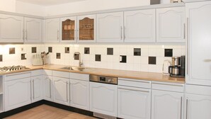 Una cocina con armarios blancos, un lavamanos de acero inoxidable, una estufa y una cafetera.
