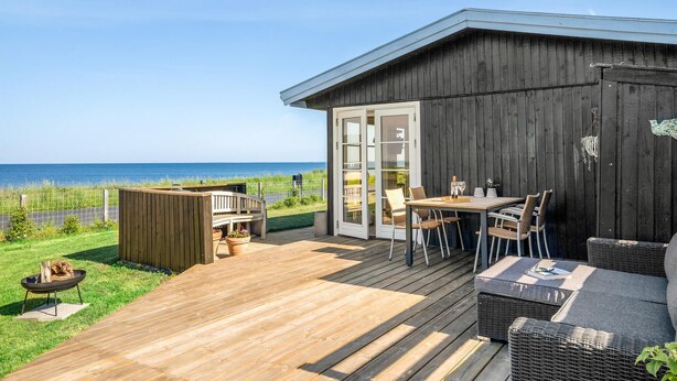 A wooden deck with a table and chairs, a fire pit, and a view of the sea. - 1 bedroom lovely home in Slagelse (Slagelse)