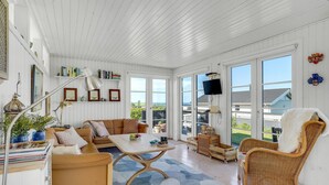 A bright, open-plan living area with a high ceiling, large windows, a sofa, a dining table, and a wicker chair. - 1 bedroom lovely home in Slagelse (Slagelse)