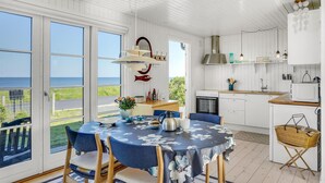 A coastal home with a dining area featuring a table with a floral tablecloth, a kitchen with white cabinets, and a view of the sea. - 1 bedroom lovely home in Slagelse (Slagelse)