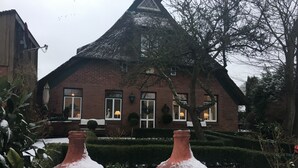 A traditional brick house with a steeply pitched roof, a well-maintained garden, and a bench in front.