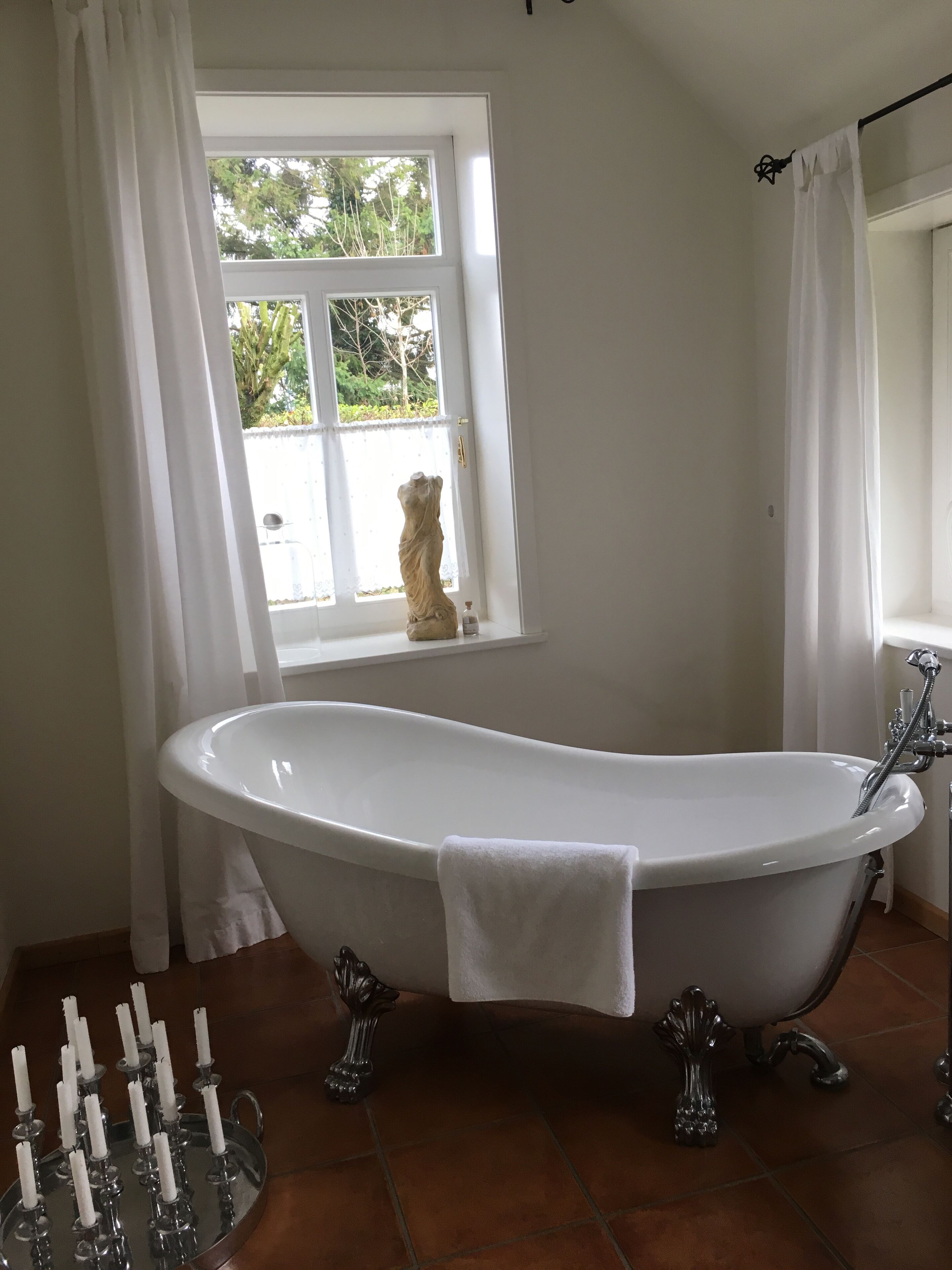 A bathroom with a freestanding bathtub, a window with a view of greenery, and a tray with candles.