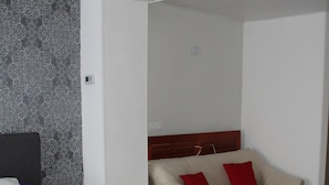 A hotel room with a bed, a sofa, a nightstand, and a wall with a patterned design. - Cozy cottage on the vineyards (Lieser)