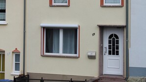 A two-story residential building with a beige facade, a white door, and a small front porch with steps. - Cozy cottage on the vineyards (Lieser)