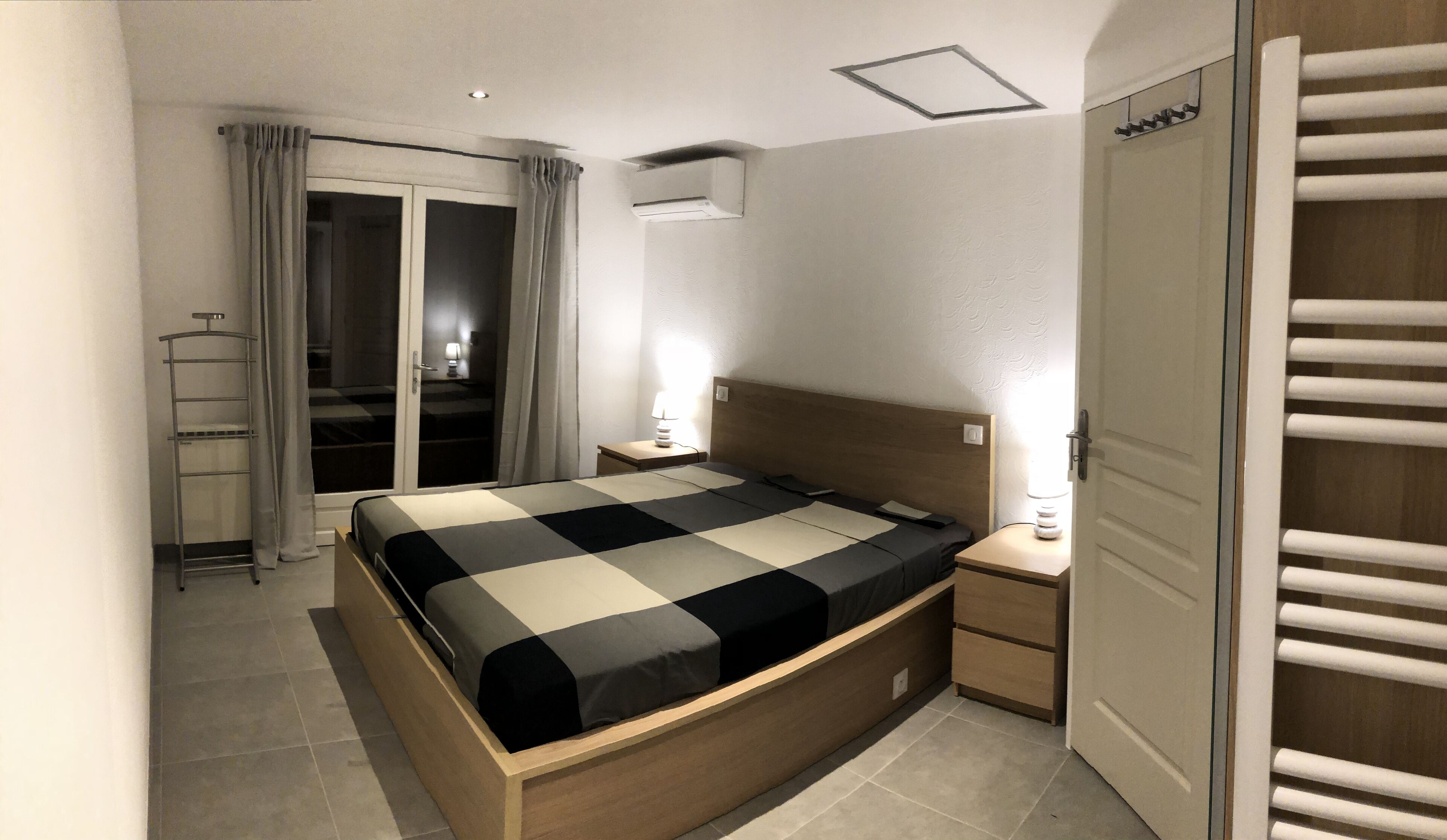 Un dormitorio moderno con cama, mesitas de noche, armario y balcón con cortinas.