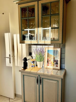 A kitchen with a cabinet containing glassware and a potted plant.