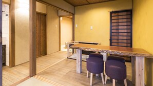 A room with a wooden floor, a long table with two purple stools, and a window with horizontal blinds. - Ichijyo-Karin (Kyoto)