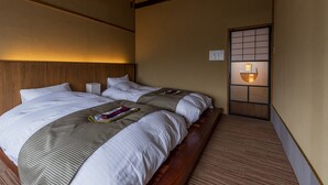 A hotel room with two beds, wooden headboards, a traditional Japanese sliding door, and a ceiling fan. - Ichijyo-Karin (Kyoto)