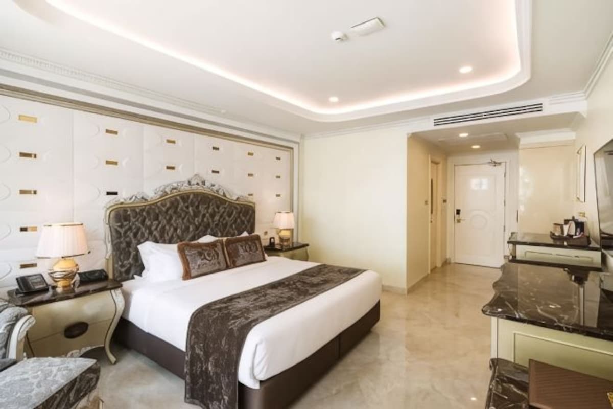 A spacious bedroom with a large bed, bedside tables, a vanity, and a mirror.