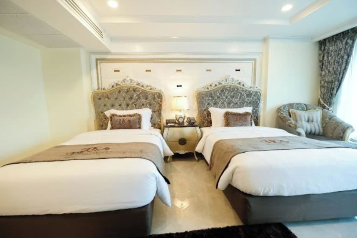 A hotel room with two beds, a nightstand between them, and a chair.