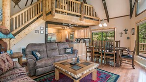 A spacious living area with a wooden staircase, a sofa, a coffee table, and a dining set.