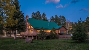 A lodge with a green roof, a stone chimney, and a deck.