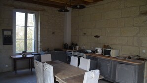 Uma cozinha rústica com parede de pedra, vigas de madeira no teto, uma janela grande e eletrodomésticos simples.