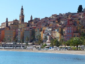 Eine Küstenstadt mit bunten Häusern, einem Strand mit Sonnenschirmen und einem markanten Kirchturm.