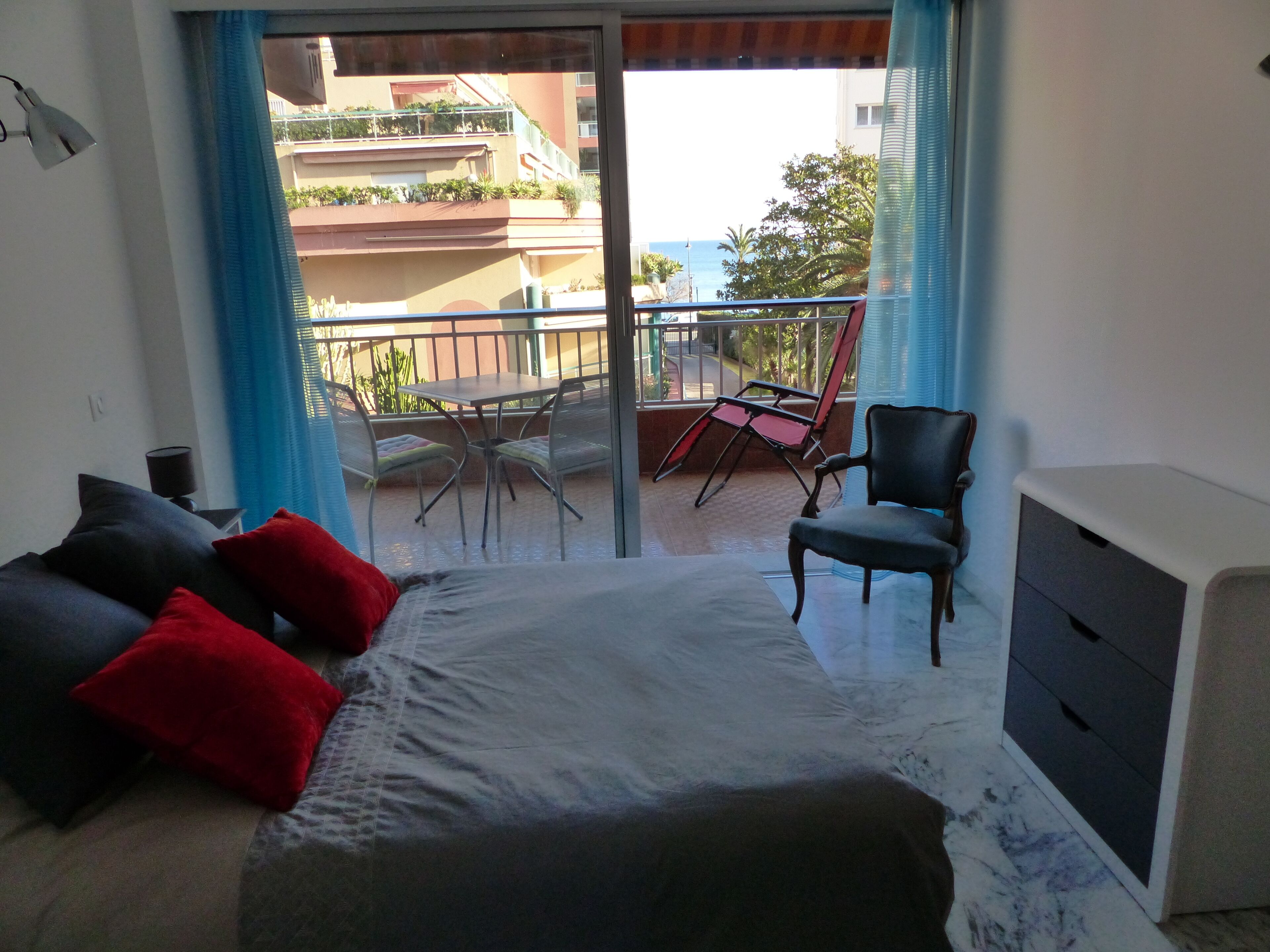 A bedroom with a bed, a desk, a chair, and a balcony with a table and chairs.