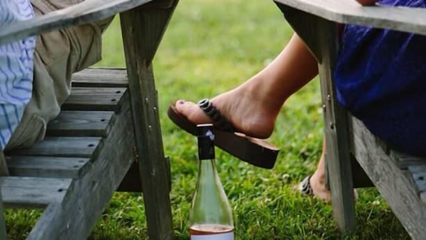 Deux personnes sont assises à une table en bois à l’extérieur et tiennent chacune un verre contenant une boisson.