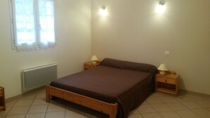 A bedroom with a wooden bed, two bedside tables with lamps, a radiator, and a window with curtains.