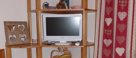 A wooden TV stand with a flat-screen TV, shelves with decorative items, and a red heart-patterned curtain.