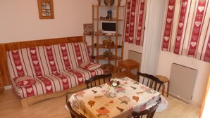 Un salon chaleureux avec un canapé, un meuble TV en bois et une table à manger recouverte d’une nappe.