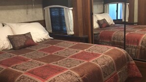 A bedroom with two beds, wooden paneling, a large mirror, and a window with curtains. - RELAX OFF THE BEATEN PATH! (Terlingua)