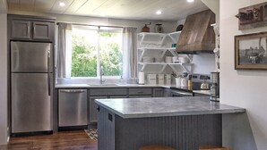 Une cuisine moderne dotée d’un îlot central, de tabourets de bar, d’appareils électroménagers en acier inoxydable et d’une fenêtre agrémentée de rideaux.