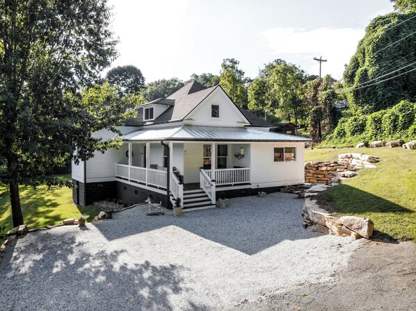 A two-story house with a porch, a stone wall, and a gravel driveway.