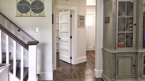 Un couloir doté d’un plancher en bois, d’un escalier et d’une armoire aux portes vitrées.