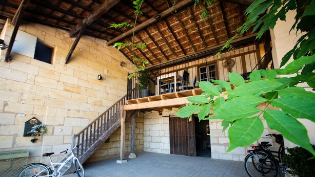 A courtyard with a staircase leading to a balcony, a white bicycle, and a potted plant. - Cottage between Bordeaux and St Emilion with Magnificent Park, surrounded by Vines (Génissac)